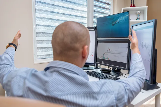 A stock trader in an office raises his hands in celebration while monitoring multiple screens with financial charts. Så räknar du företag per bransch med offentlig statistik